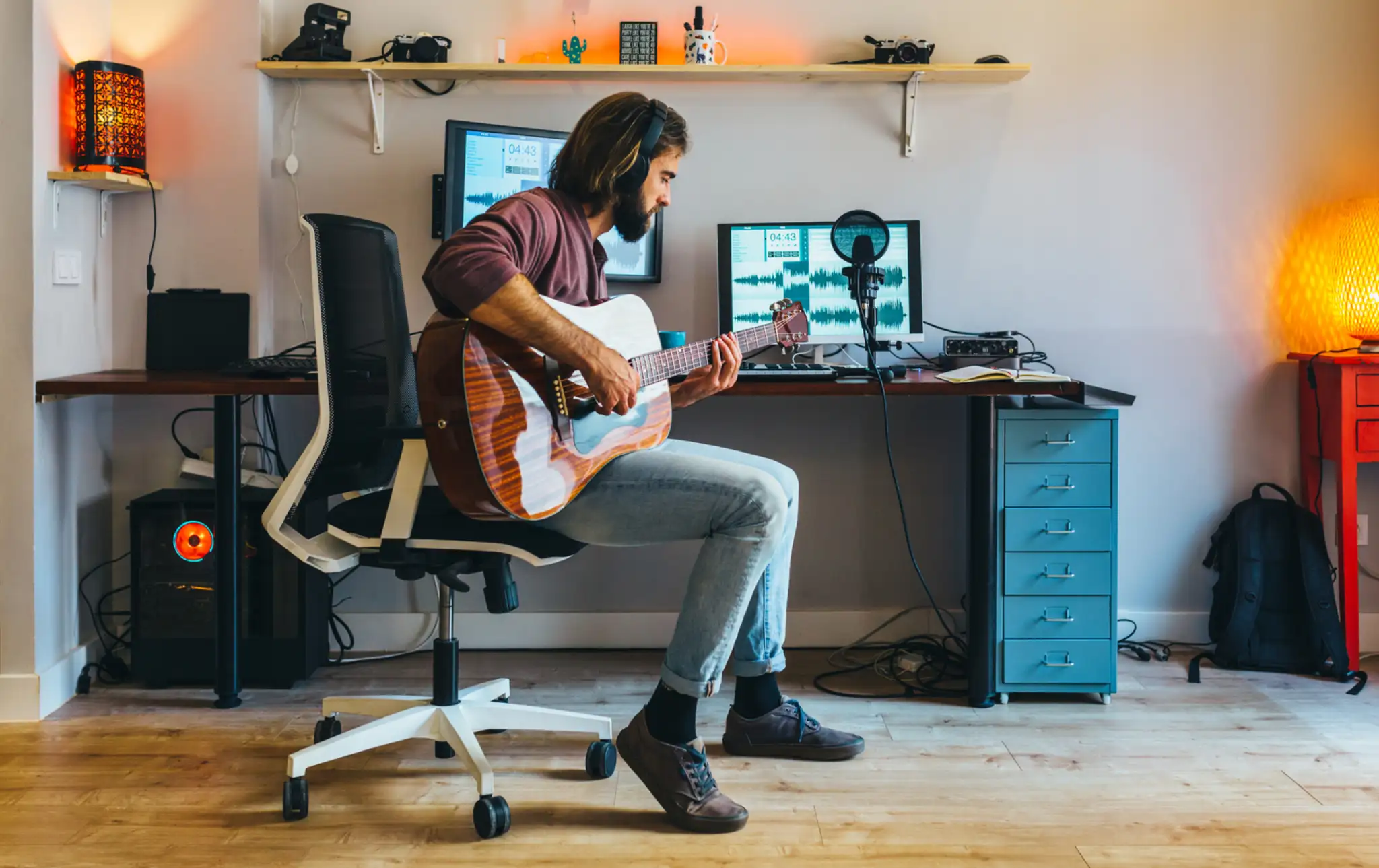 Sitting musician with guitar in front of a desk with computer